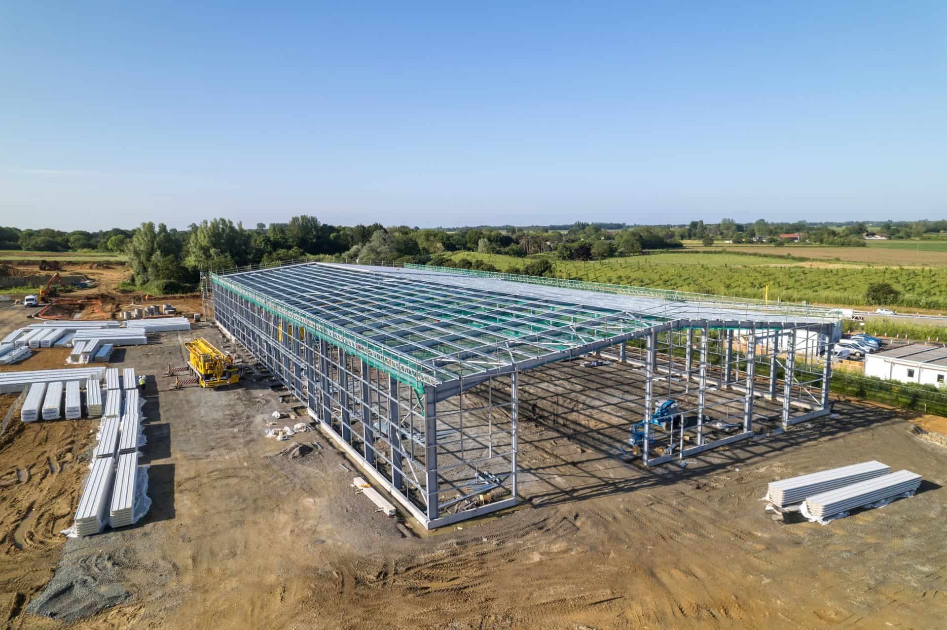Aerial view of a steel-framed warehouse under construction with safety netting